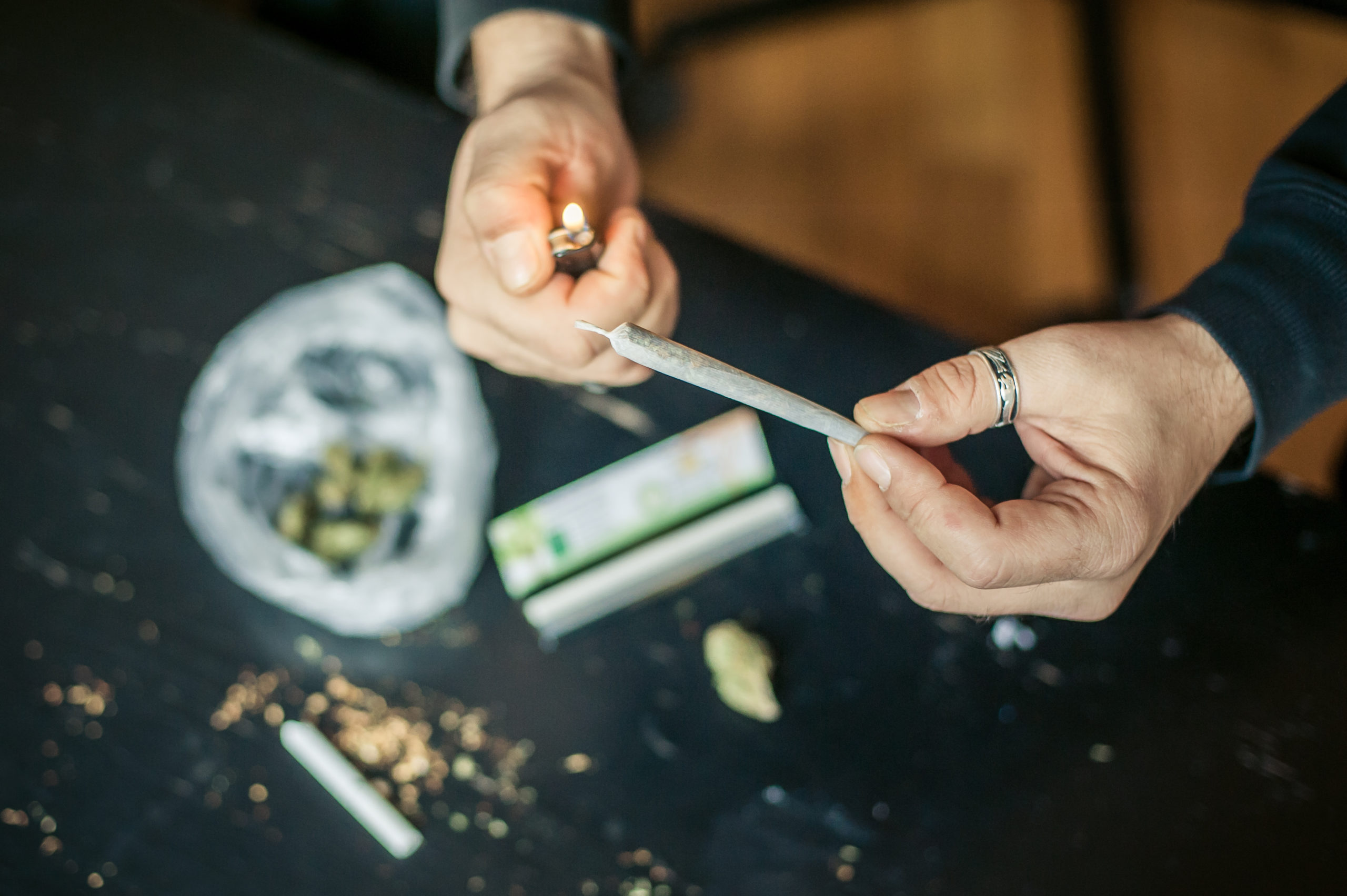 A man holds a lit lighter up near the end of a cannabis joint.
