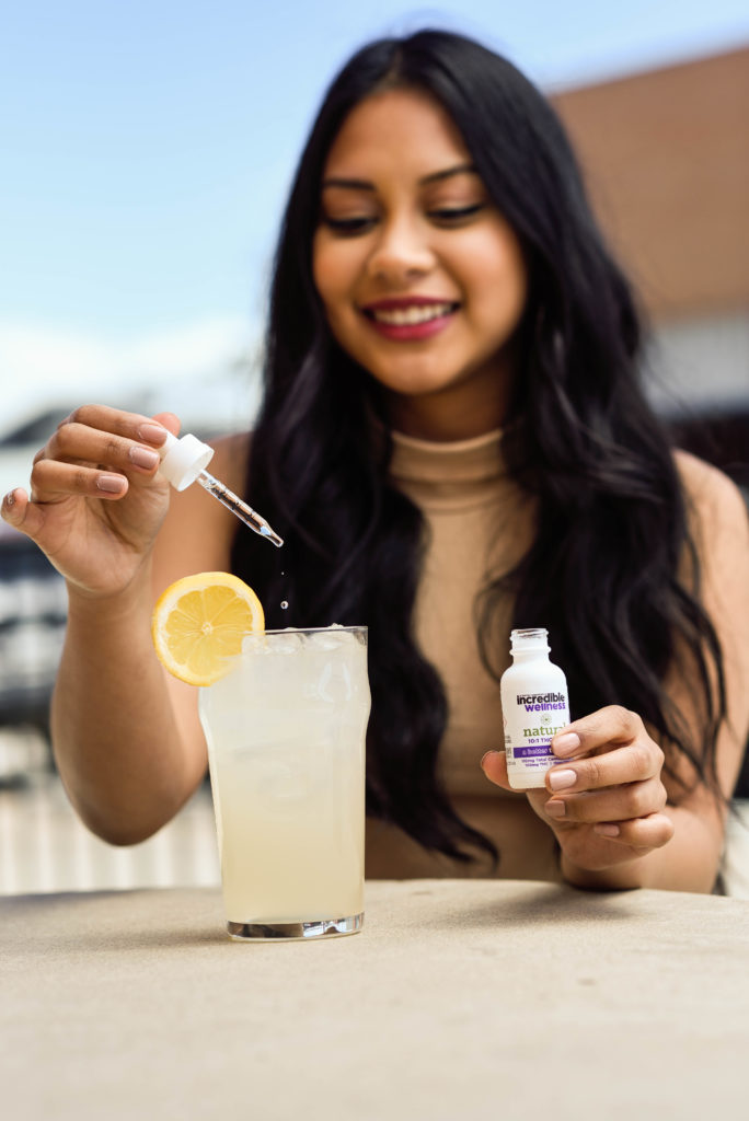 A woman dripping incredible Wellness cannabis tincture into a tall glass of lemonade for anxiety