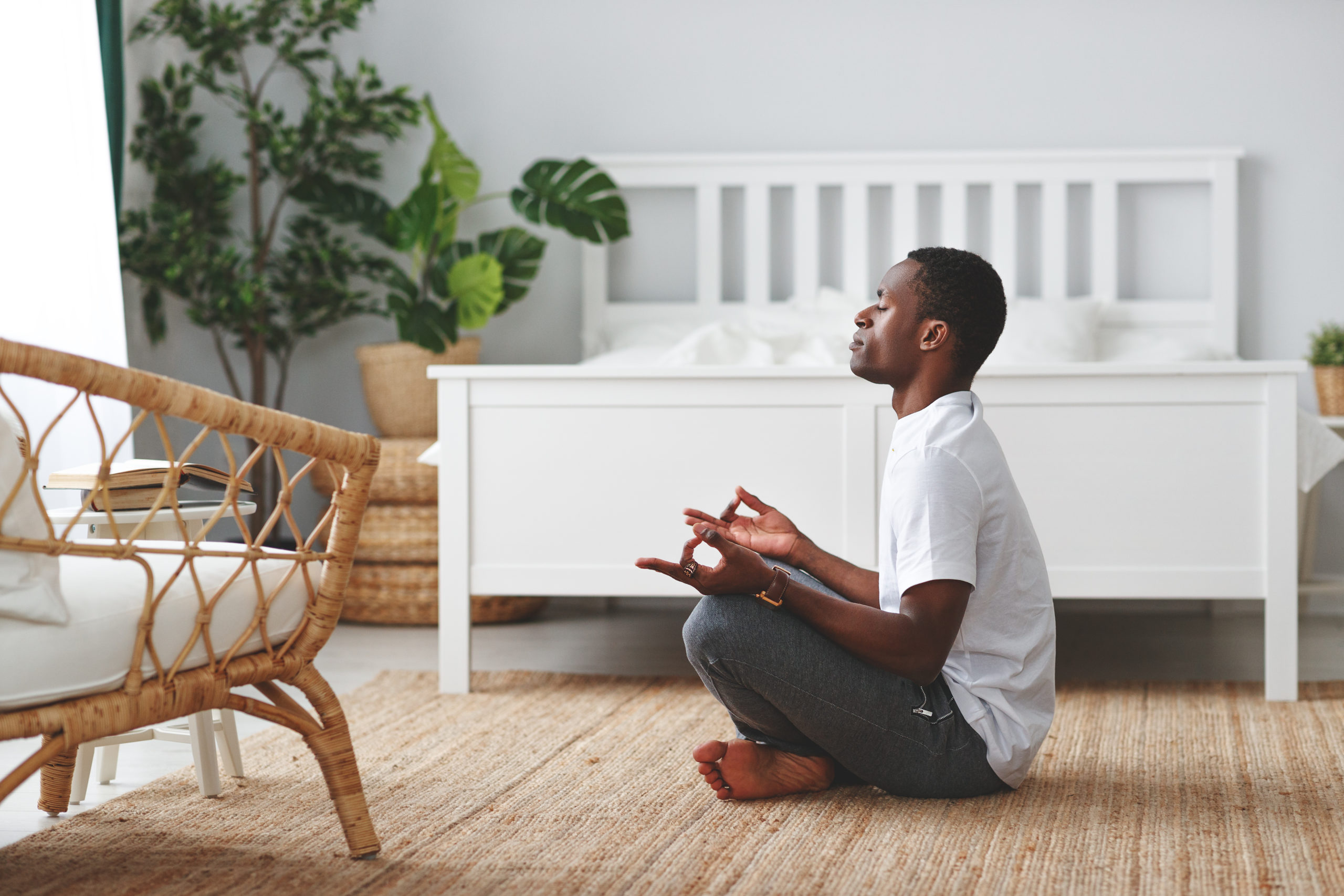 young black man doing yoga and sitting in lotus position at home in bedroom