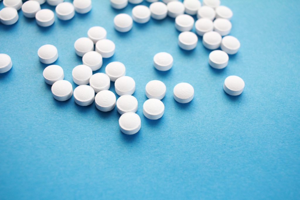 A picture of white opioid pills on top of a blue table to demonstrate the potential for cannabis to replace opioids and help chronic pain sufferers