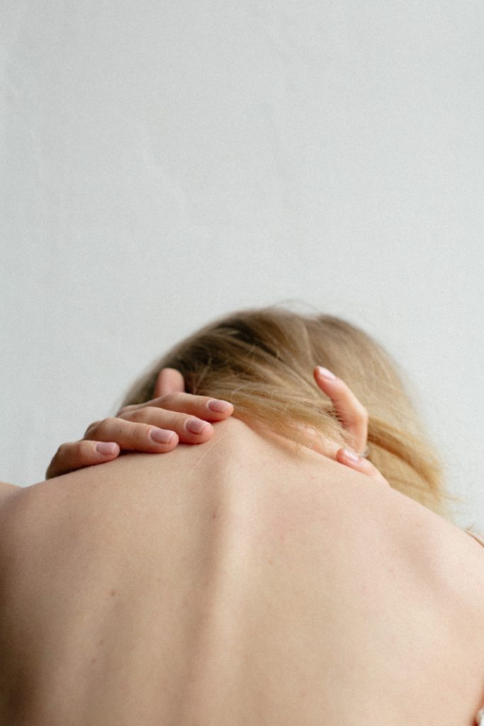 Woman with blonde hair and pink nails holding her neck in pain before consuming cannabis for pain relief