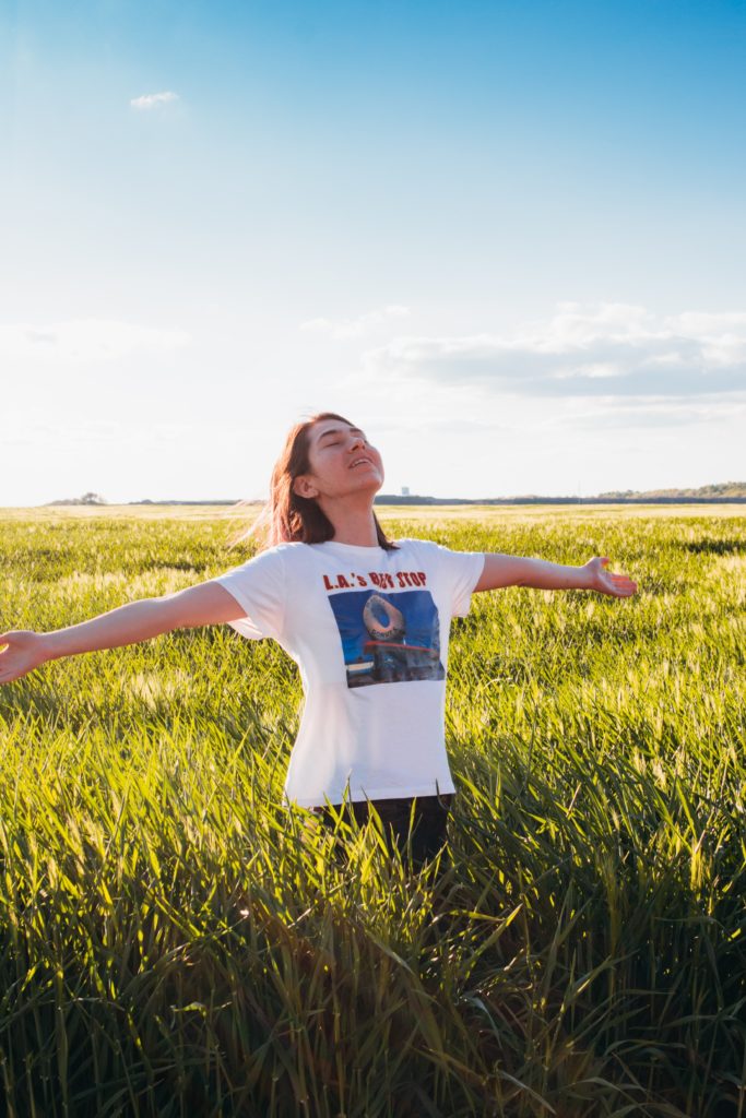 Girl with a white graphic tee standing in a meadow under the sunshine after consuming cannabis for pain
